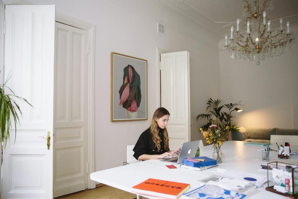 Modern home office setting with a woman working on a laptop, surrounded by decor and indoor plants.